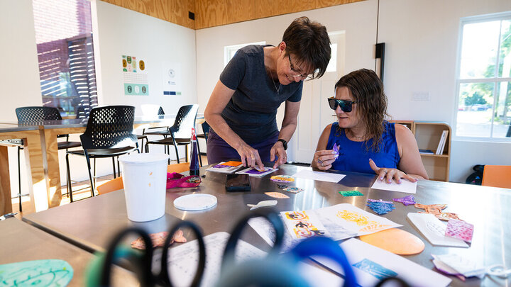 Jean Stryker (left) shows Jessica Hernandez how to dip a stamp into paint for a printmaking activity at the Art Chapel
