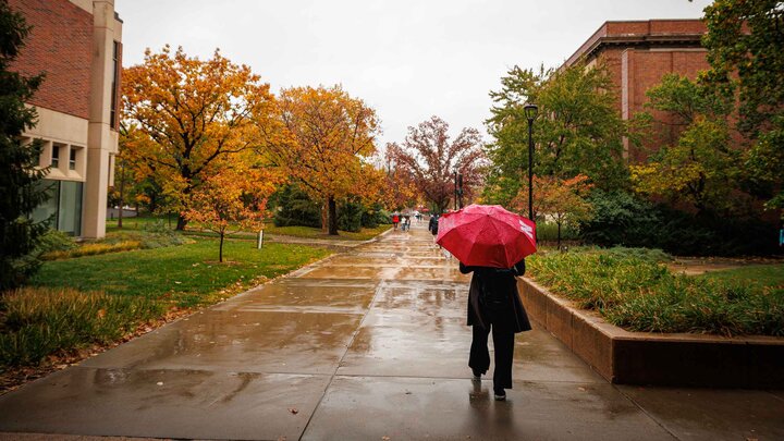person with red N umbrella walking in the rain on UNL campus